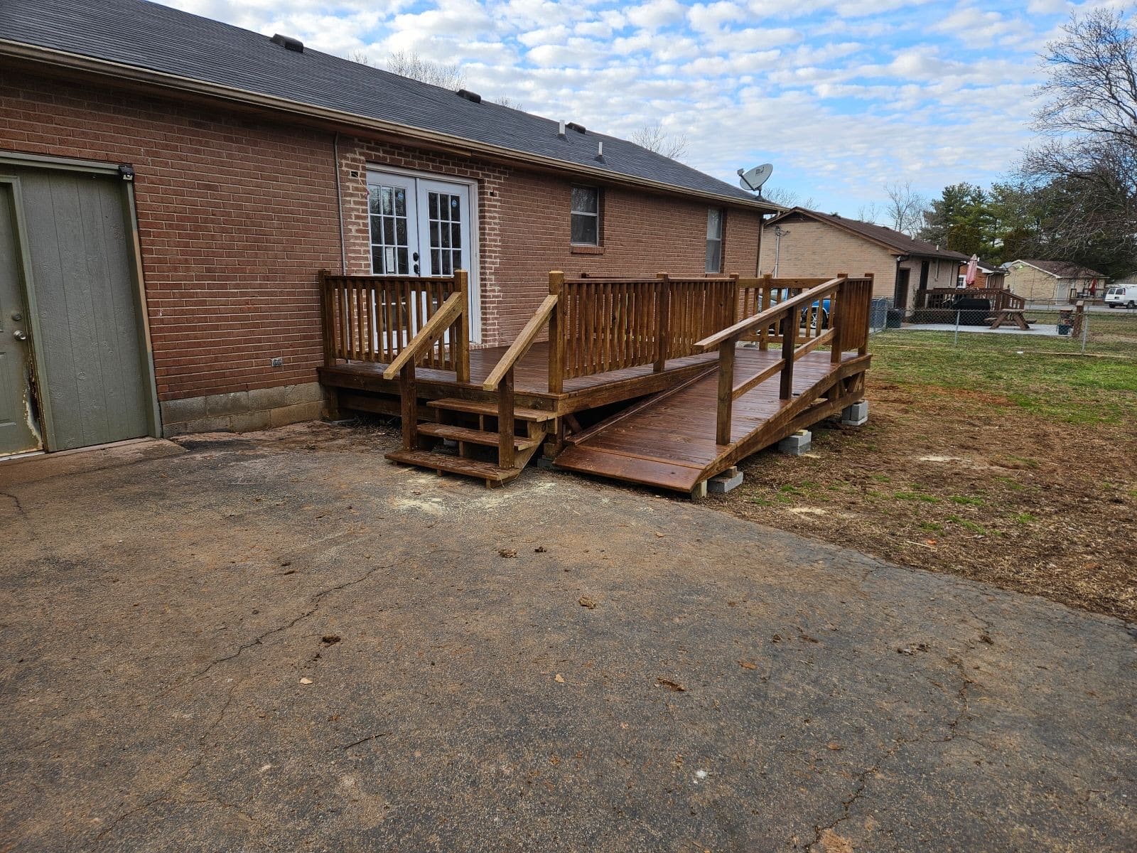 Side view of a brown-stained 10x16 deck with wooden railings and an extended ramp leading to a brick house in Murfreesboro, Tennessee.