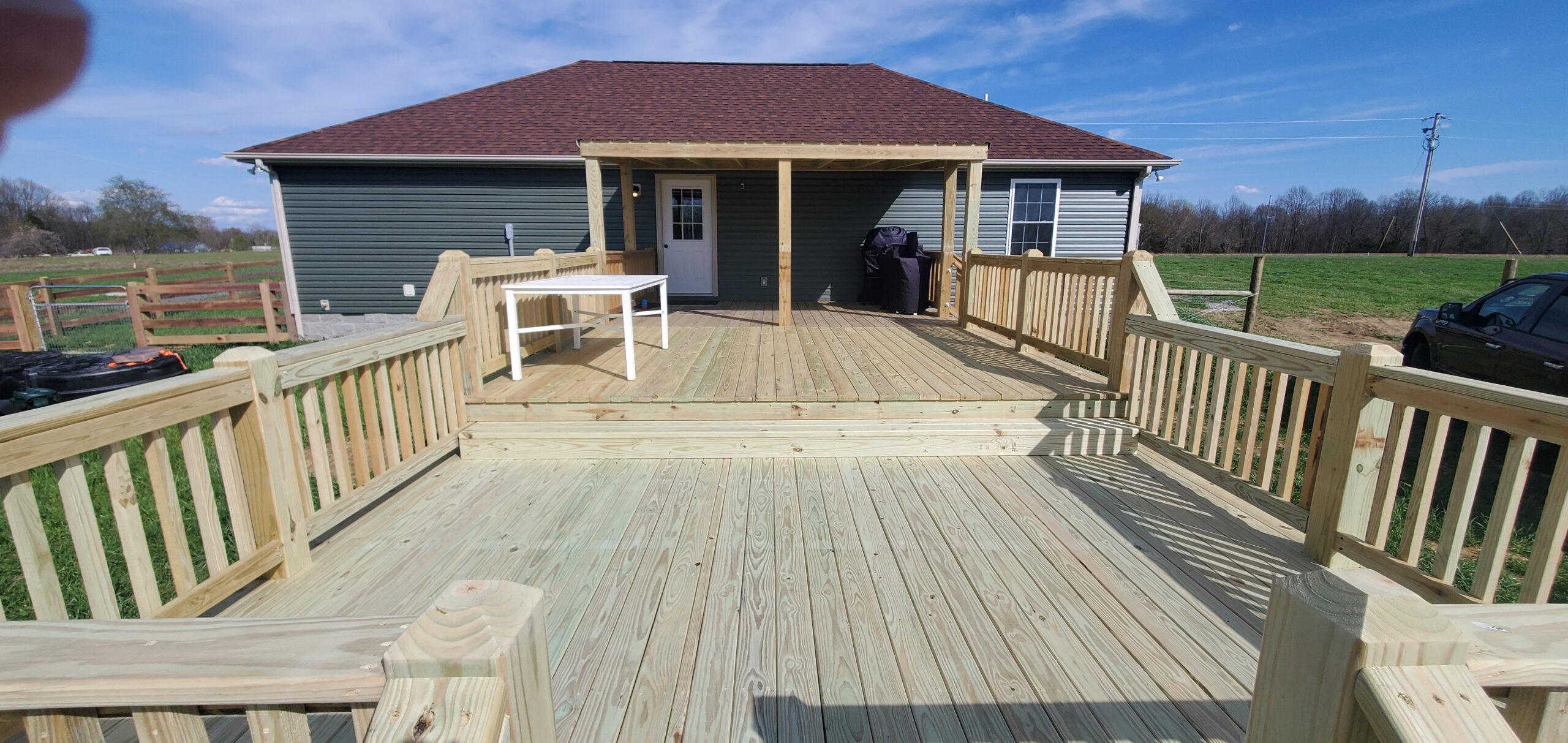 View of a spacious 24x16 backyard deck leading to a covered porch area on a green house in Westmoreland, Tennessee.