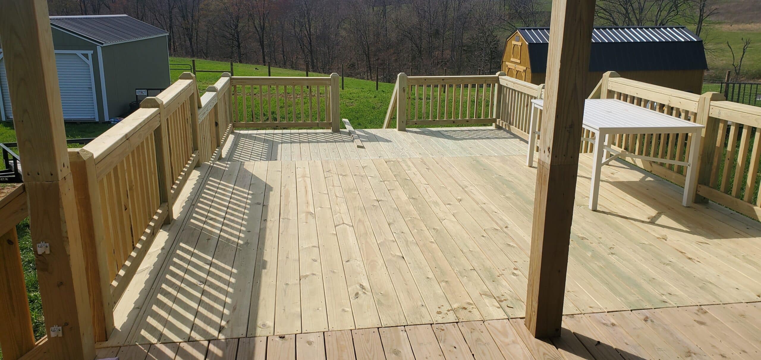 Large 24x16 wooden deck with railings and stairs attached to a green house with a covered porch in Westmoreland, Tennessee.