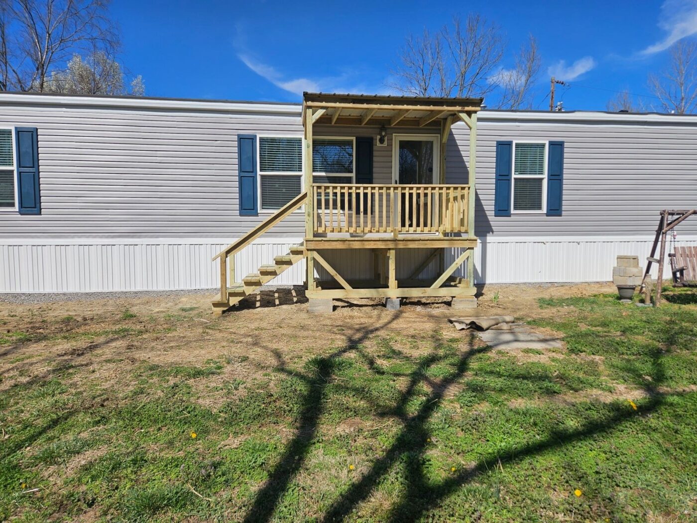 Angled view of a 6x10 covered front deck with a wooden staircase and railing attached to a light gray mobile home in Elkton, Kentucky.