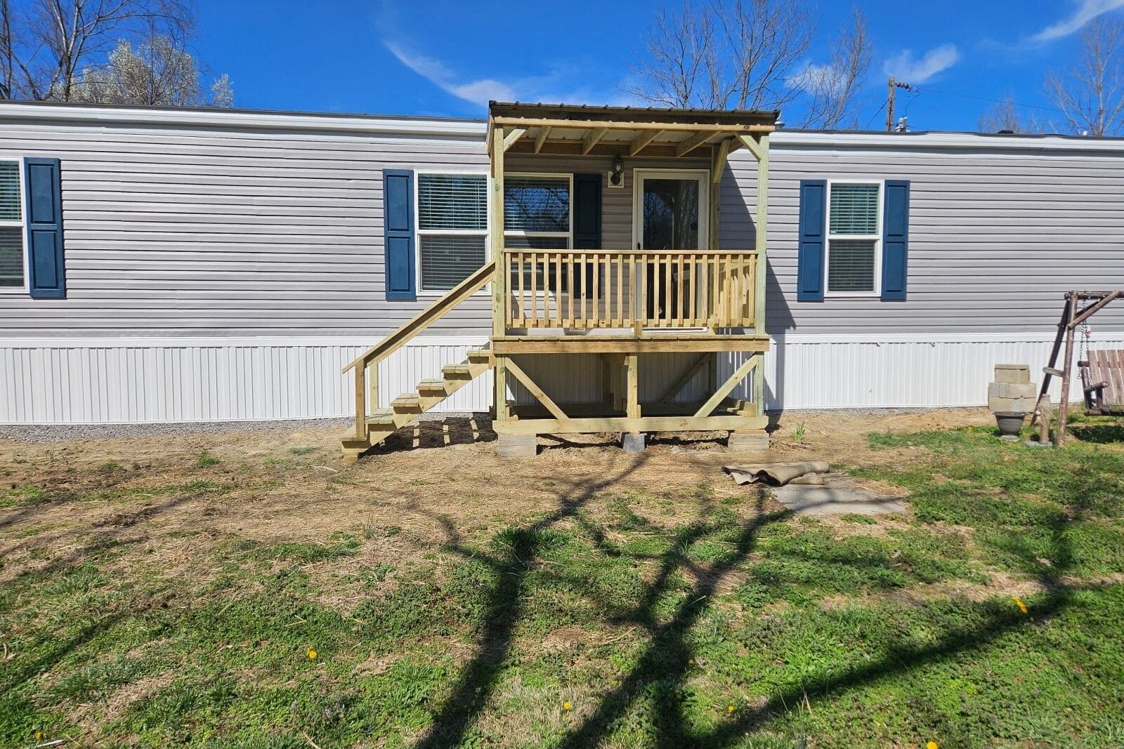 Angled view of a 6x10 covered front deck with a wooden staircase and railing attached to a light gray mobile home in Elkton, Kentucky.