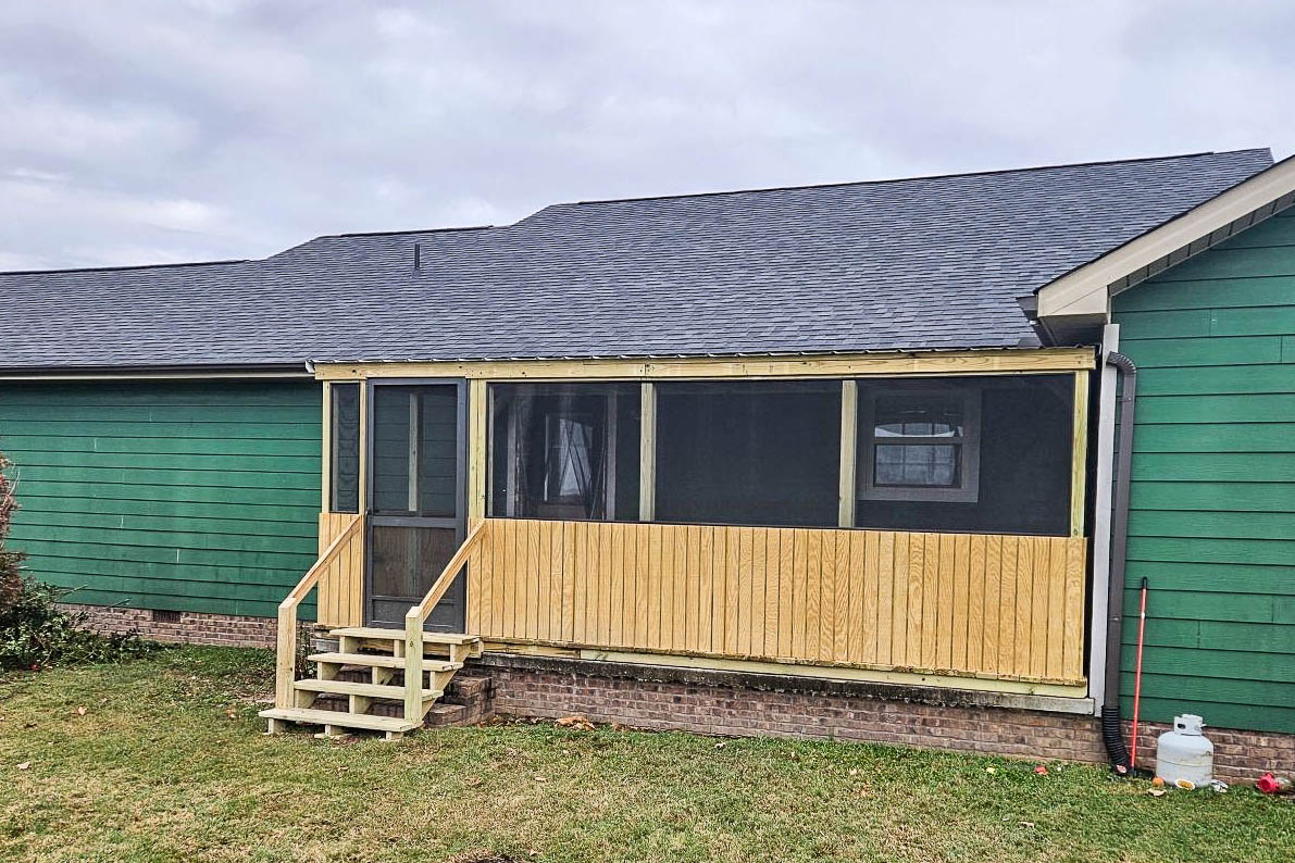 Full view of an 8x20 screened porch with front entry door and wooden steps on a green home in Rickman, Tennessee.