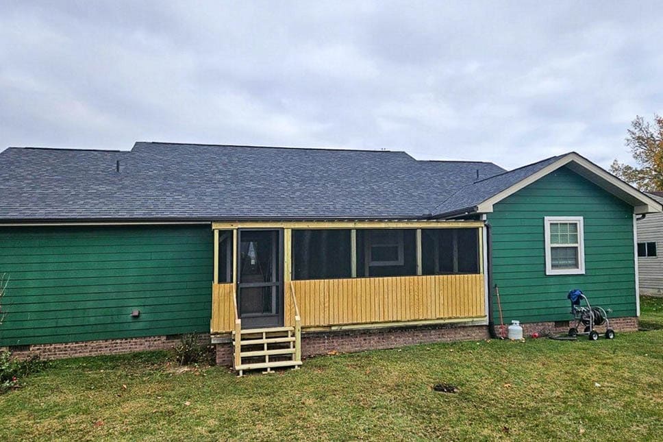 Angled view of an 8x20 screened porch with wood rails, screens, and steps attached to a green house in Rickman, Tennessee.