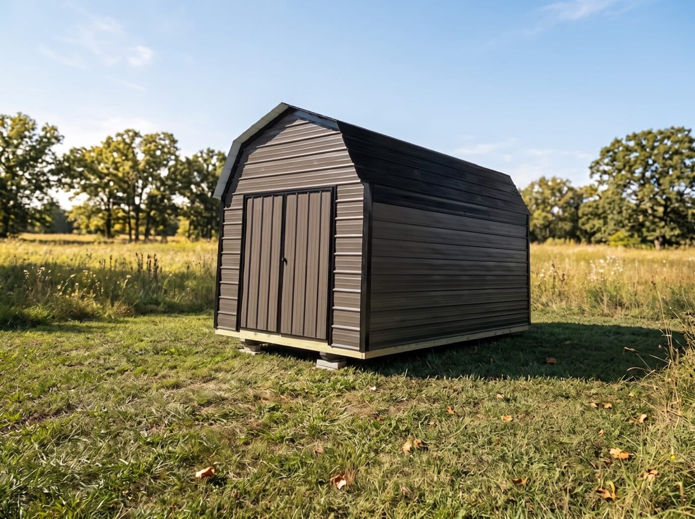 Brown horizontal metal shed with double doors and a gambrel-style roof in a grassy field.
