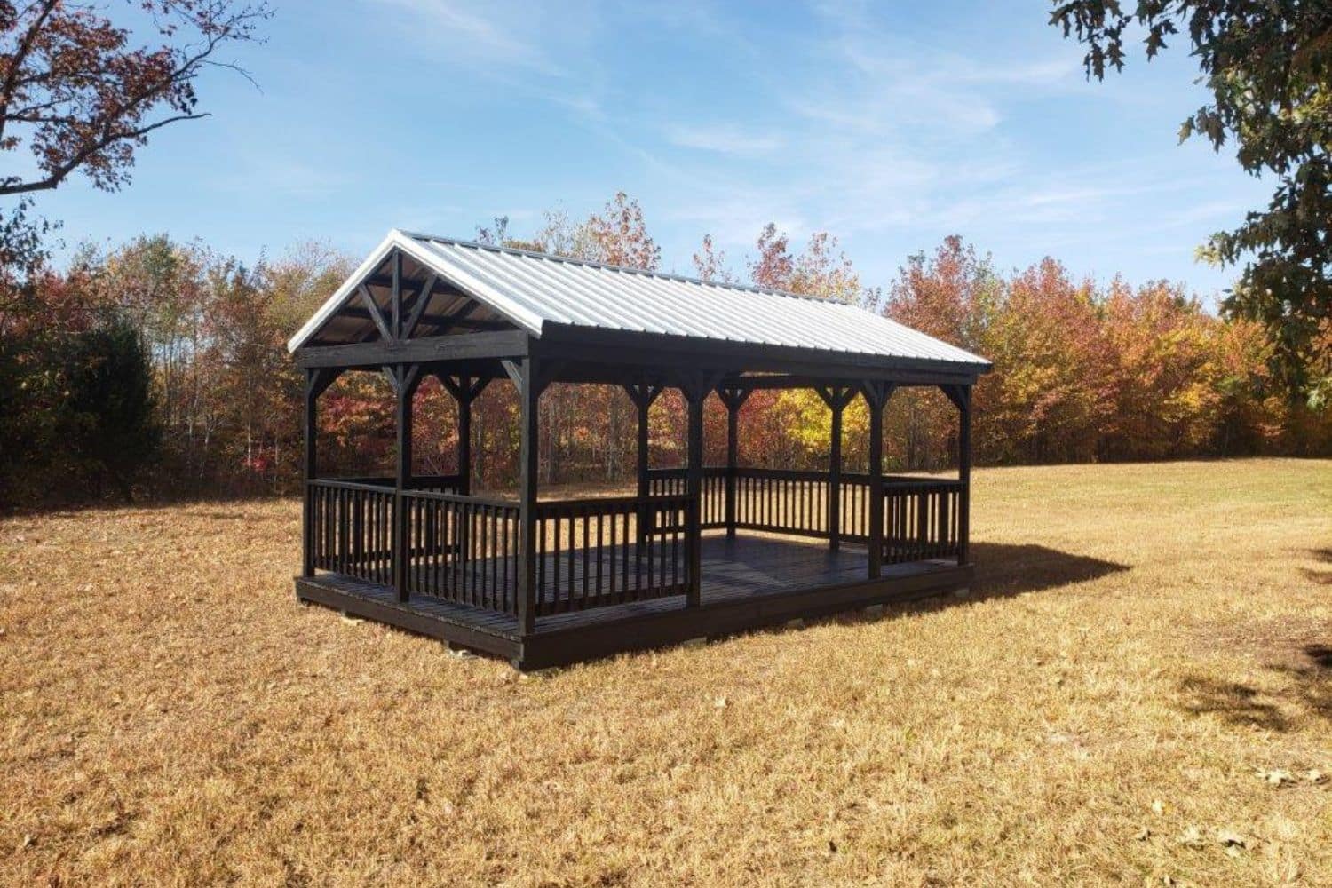 Dark stained portable pavilion with metal roof in field