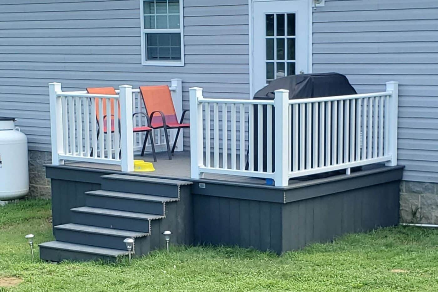 Small house deck in Kentucky with seating area and grill. Steps lead off the deck to the yard