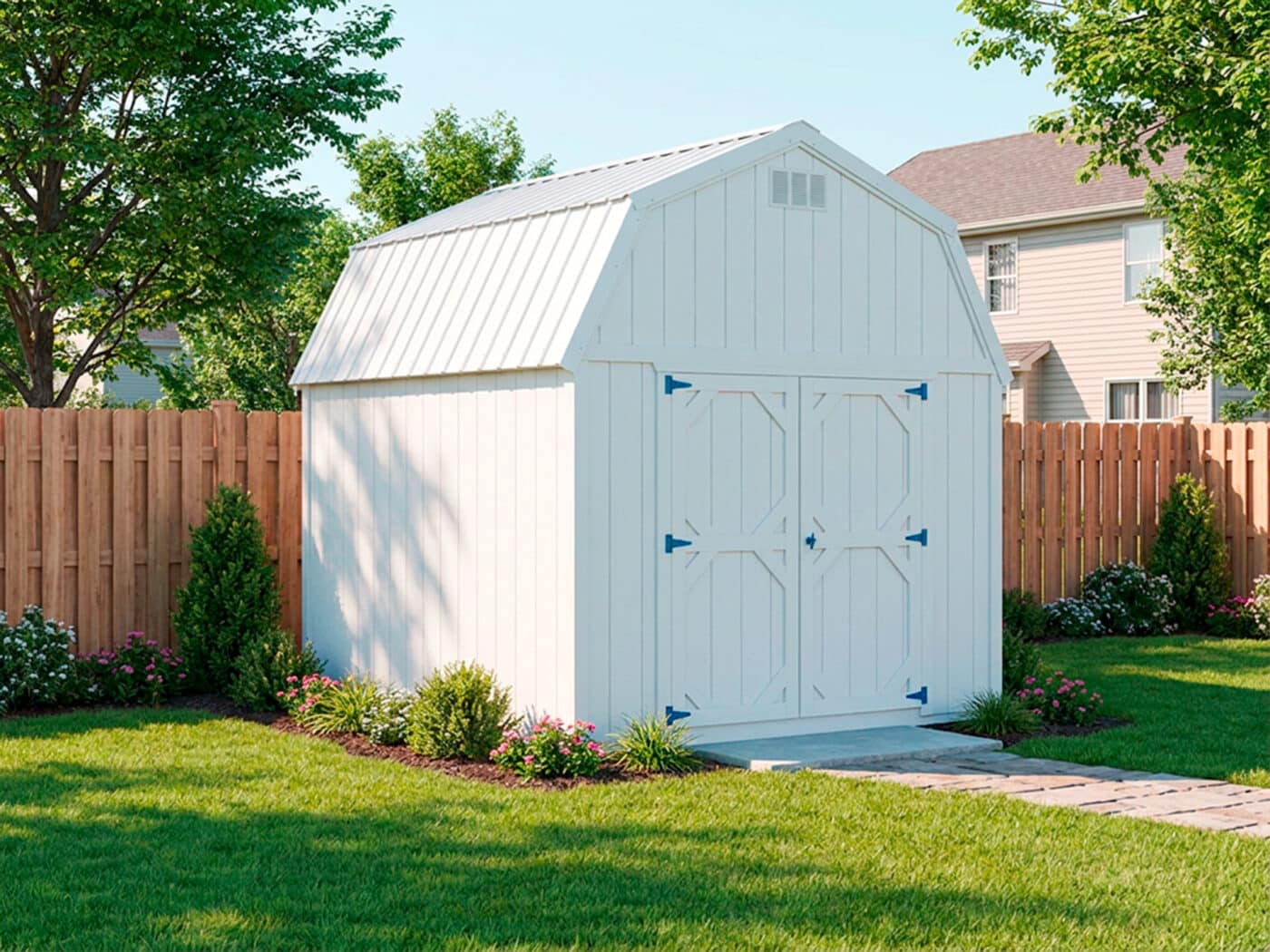 White lofted barn shed with double doors in a landscaped backyard with flowers and shrubs.