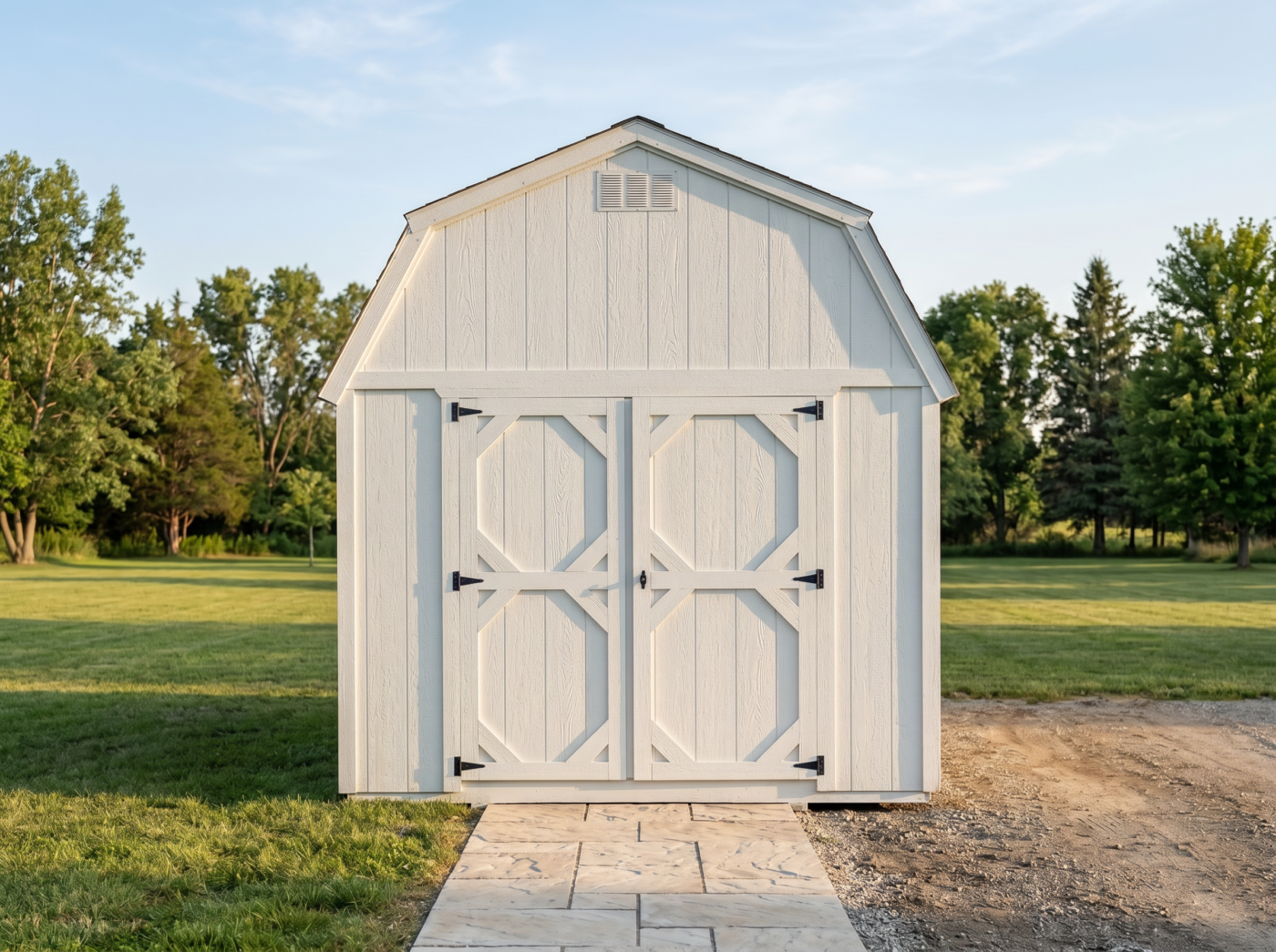 White lofted barn shed with double doors and black hardware on a grassy property.