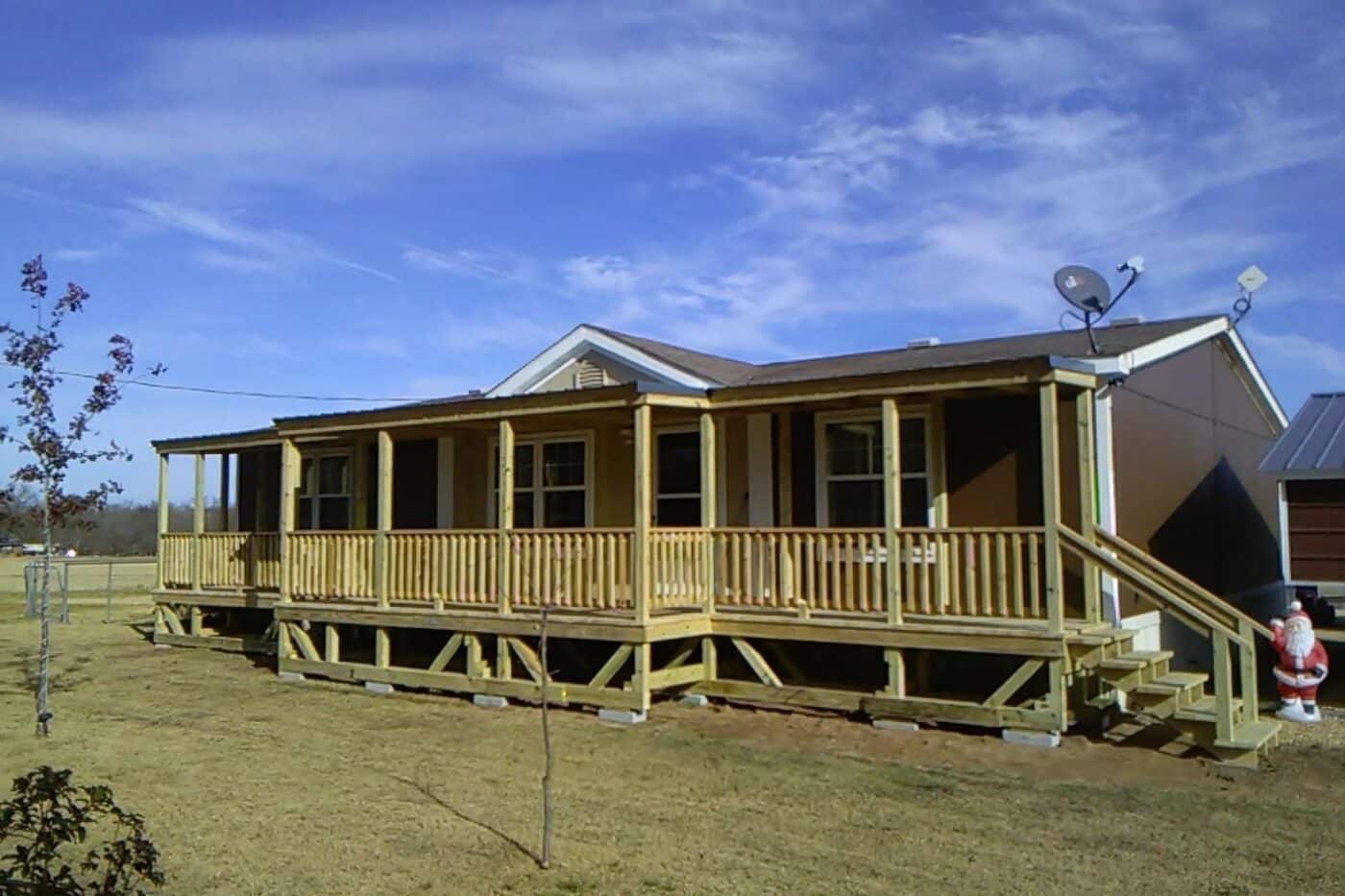 Extensive porch with roof, steps, and railings attached to brown mobile home with white trim