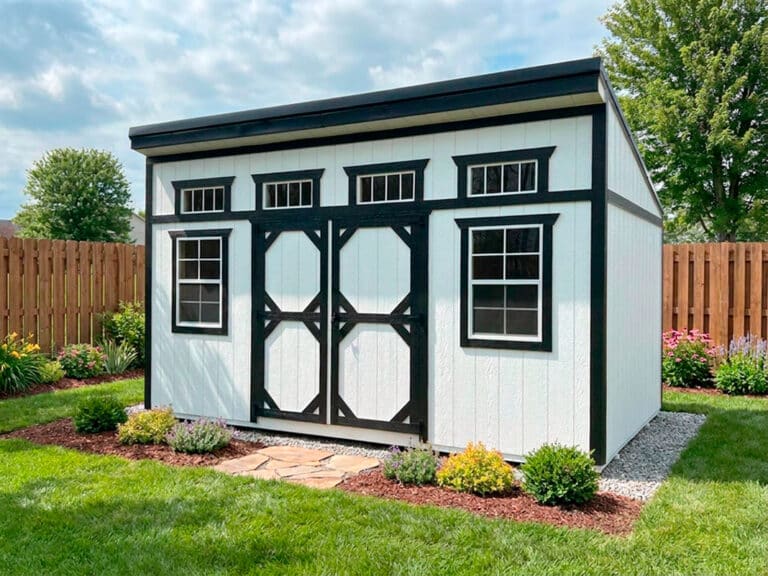 White modern shed with black trim, double doors, and front windows in a grassy field.