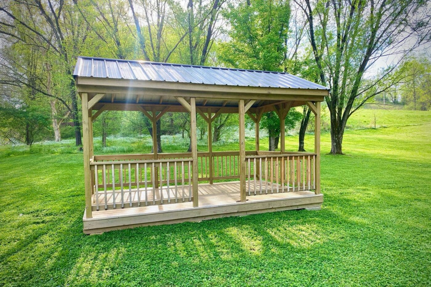 Portable pavilion in bright green grass clearing with metal roof and wooden railing