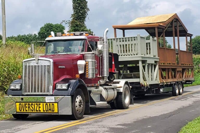 Prebuilt EshCo structures on truck with overload sign on road in front of cornfield