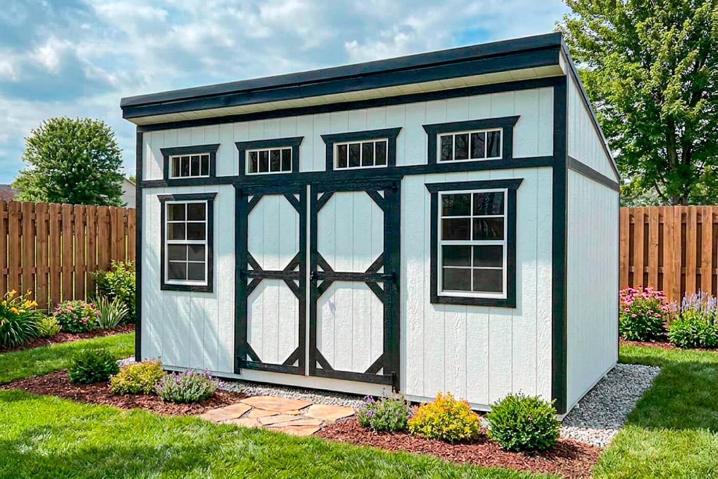 White modern shed with black trim, double doors, two front windows, and four transom windows in a landscaped backyard.