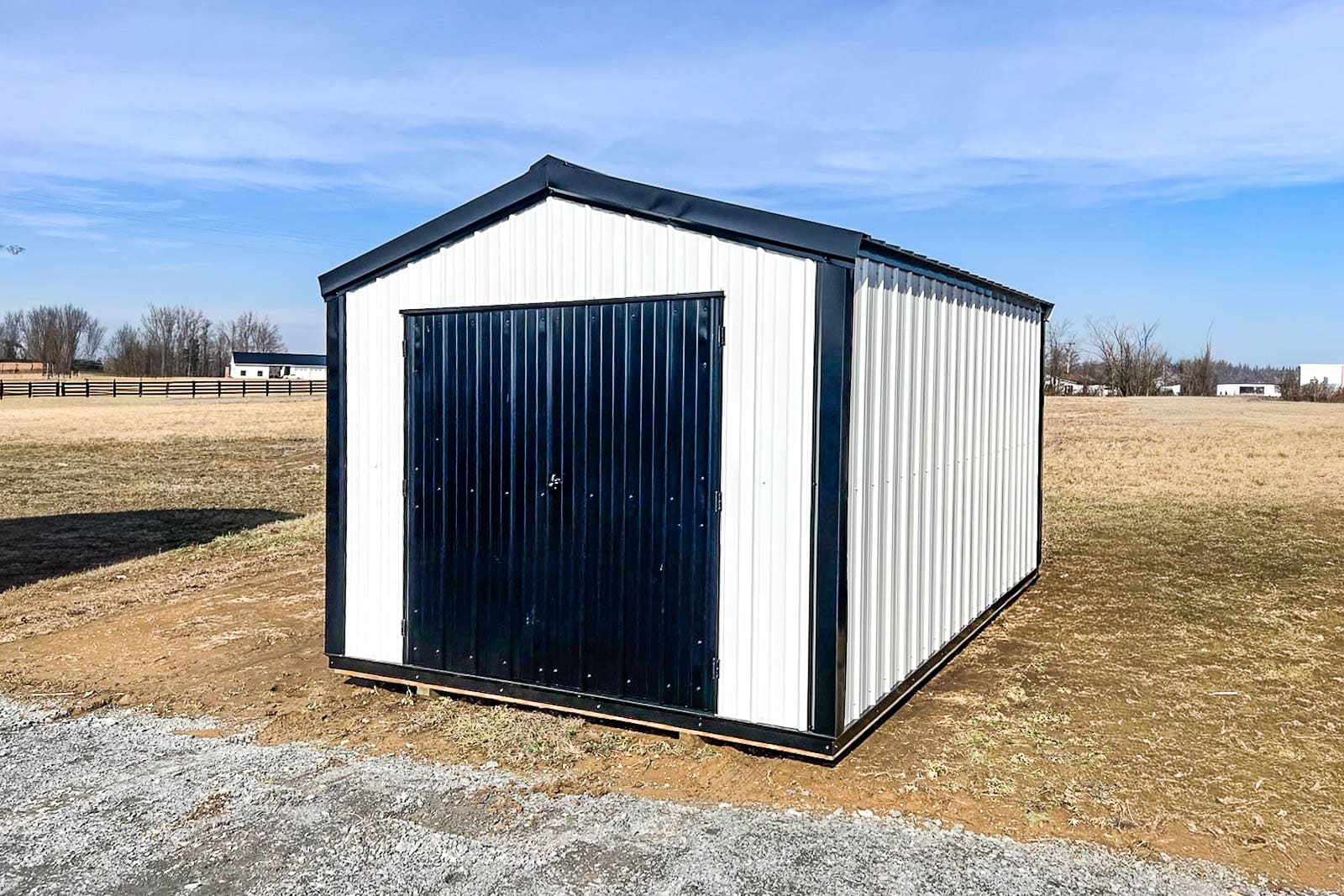 White metal storage shed with black trim and wide black double doors in an open field.