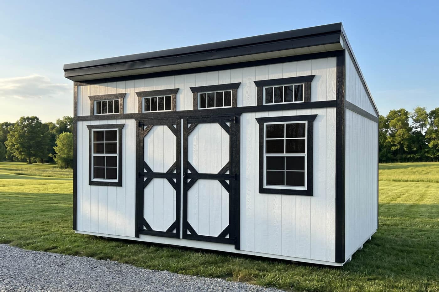White modern shed with black trim, double doors, two windows, and four transom windows in a grassy rural setting.
